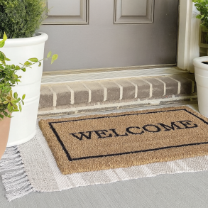 Kokosm�tte med teksten &ldquo;WELCOME&rdquo; placeret foran en hovedd�r, omgivet af gr�nne potteplanter &ndash; holdbar og stilren udend�rsm�tte fra T�ppetossen.